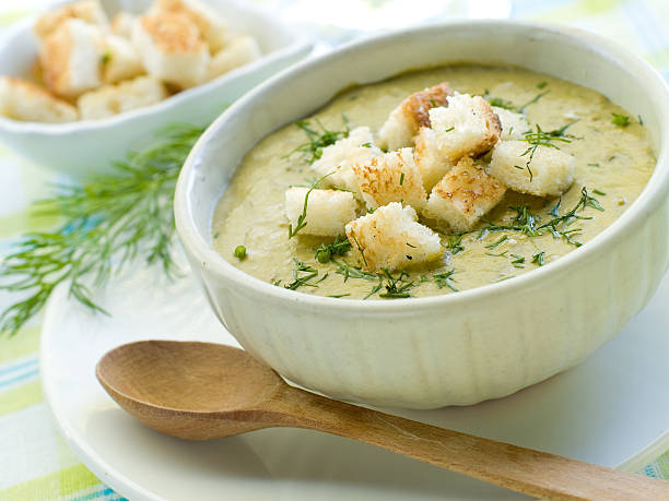 White bowl of soup with croutons next to a wooden spoon stock photo