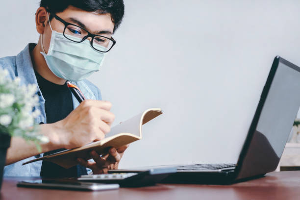 istock Asian man wear a mask to protect against Corona virus. New normal Working and e-learning, Checking Use smartphones and laptops to work at home. SME Business Plan, Working from home ideas 1245761108