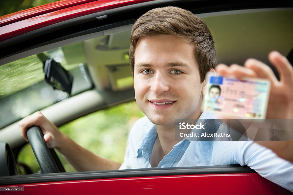 drivers license teenager sitting in new car and shows his drivers license Driver's License Stock Photo