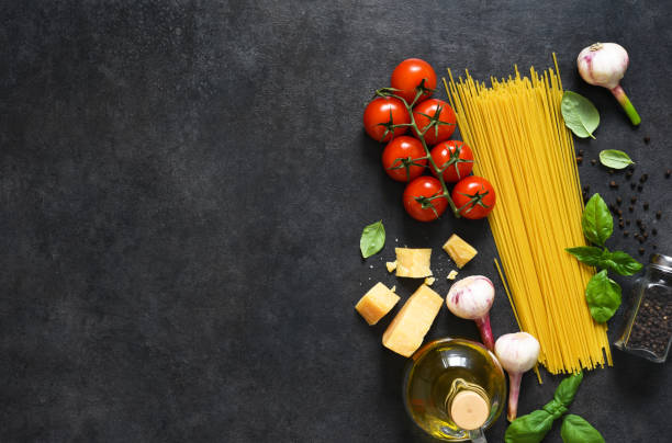 istock Ingredients for making pasta. Raw spaghetti with tomato and basil on a black background. View from above. 1245830818