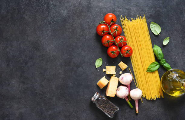 istock Ingredients for making pasta. Raw spaghetti with tomato and basil on a black background. View from above. 1245830822