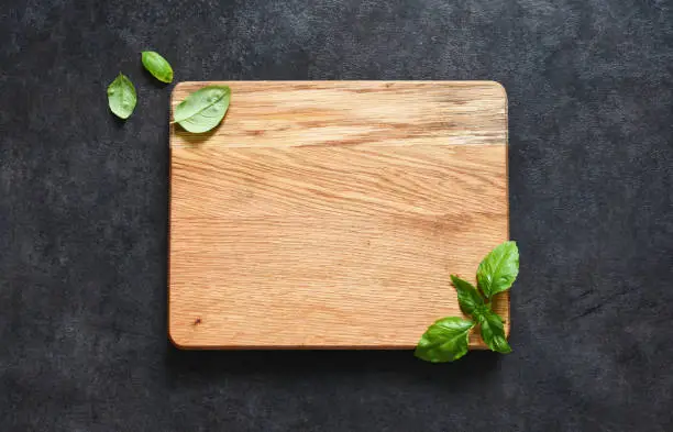 Photo of Cutting board and basil on a black stone background. Food background with place for text. View from above