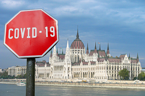 Covid-19 sign with parliament building in Budapest, Hungary. Coronavirus pandemic outbreak concept.