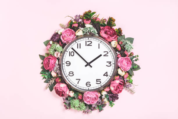 istock Part of wall clock in blooming flowers on candy pink background 1245883172