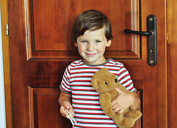 A teddy is hanging on a wooden door handle with carved design background, the stuffed bear is looking nice with the wooden cupboard which is hanging on the door, the handmade bear is looking very clear and bright in the room.