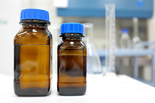 No label amber glass bottle with clear liquid chemical inside a laboratory with copy space.