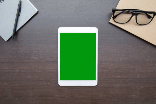 Work space desk table top overhead place tablet green screen at center layout left right have notebook glasses and pen