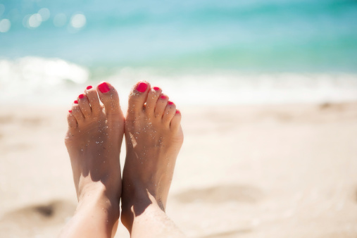 Close up of woman feet laying on white sand beach with blue sky and shining sun at background. Copy space.