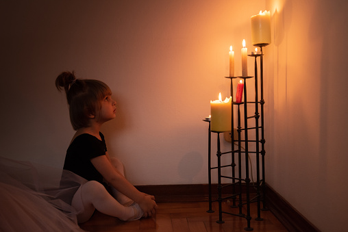 Side View of Little Girl Sitting on Floor Looking at Burning Candles with Awe