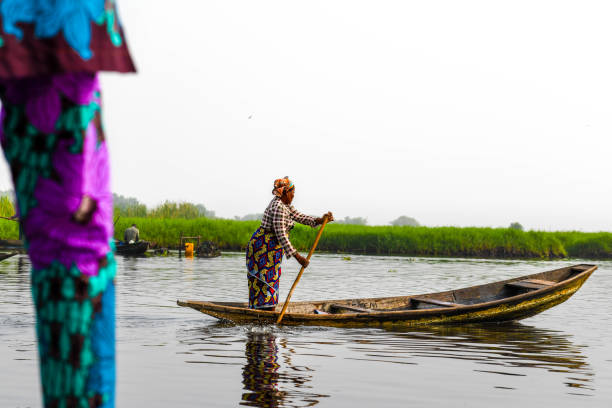 A woman stands on a pirogue on Lake Nokoue. Africa, West Africa, Benin, Lake Nokoue, Ganvié. A woman stands on a pirogue on Lake Nokoue. benin stock pictures, royalty-free photos & images