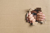 Little Girl Peeking From A Hole On Cardboard Box. Concept Of A Human Trafficking And Curiosity