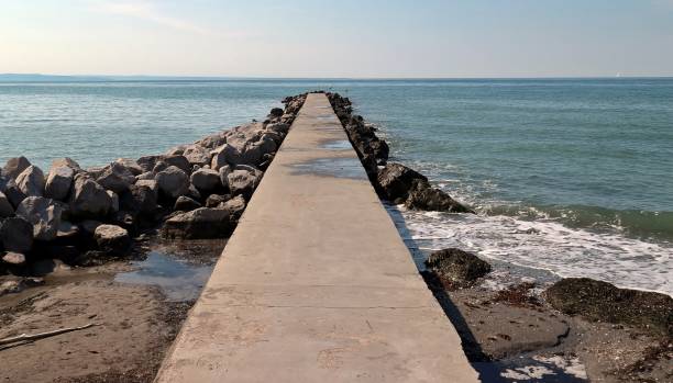 molo marino in cemento, circondato da rocce, che si estende nel mare. nessuna gente - sea defence concrete foto e immagini stock