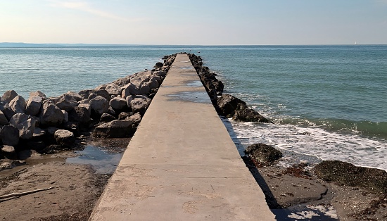 Marine concrete pier, surrounded by rocks, stretching into the sea. No people, background for copy space