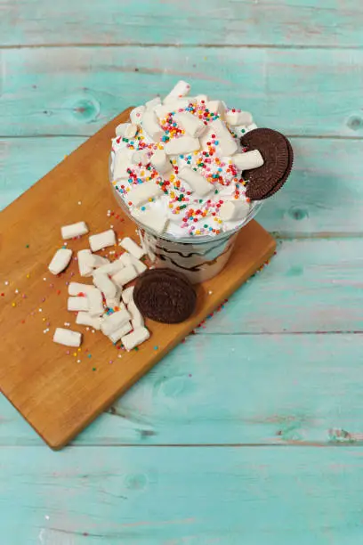 Photo of delicious sweet delicious drink with marshmallows and cookies on a wooden blue background top view. beautiful cocktail with whipped cream in still life