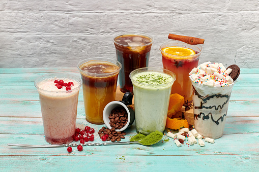 colorful bright and beautiful drinks with milk and ice stand in transparent plastic glasses on a light blue wooden background. six glasses with bright drinks and ingredients on a light background