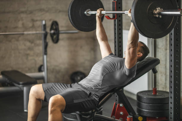 deportista haciendo prensa de banco, atleta durante el entrenamiento en el gimnasio profesional, levantamiento de pesas para bíceps, pectorales y músculos de la espalda - weight training weight bench weightlifting men fotografías e imágenes de stock