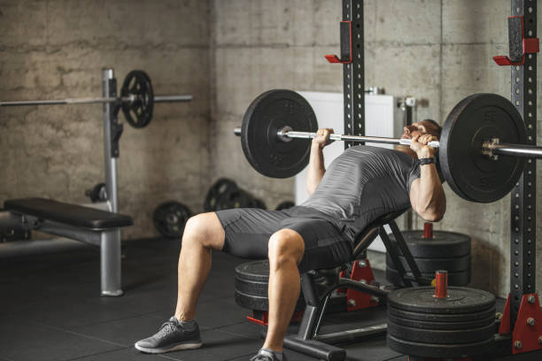 deportista haciendo prensa de banco, atleta durante el entrenamiento en el gimnasio profesional, levantamiento de pesas para bíceps, pectorales y m�úsculos de la espalda - weight training weight bench weightlifting men fotografías e imágenes de stock