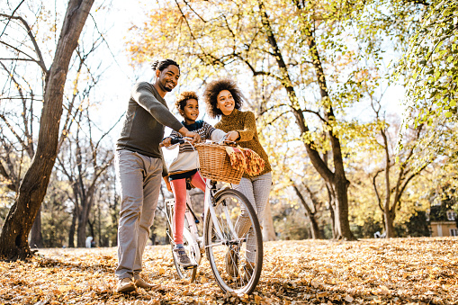 istock Padres negros felices empujando a su hija en una bicicleta en el día de otoño. 1246014077