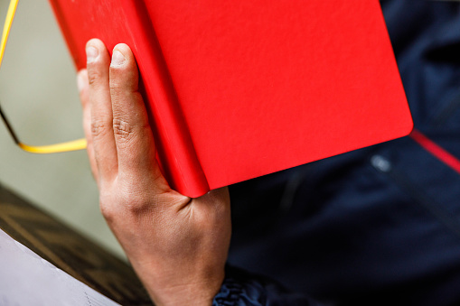 Close up of unrecognizable worker reading plans from a  red notebook.
