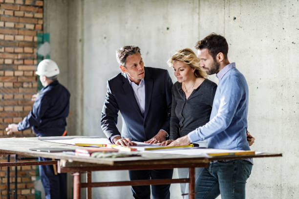 istock Young couple and their agent examining blueprints at construction site. 1246025564