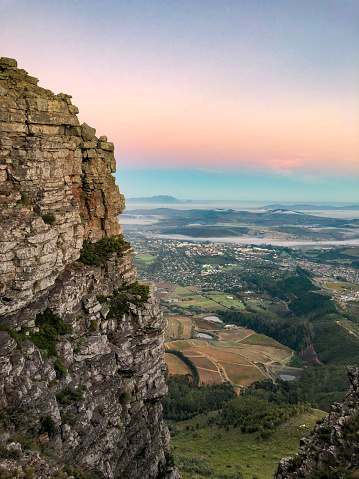A elevated distant view of Table Mountain, Cape Town from Botmaskop, Stellenbosch.  A Cape Winelands landscape scenics image at sunrise dawn.  The city is covered with fog.