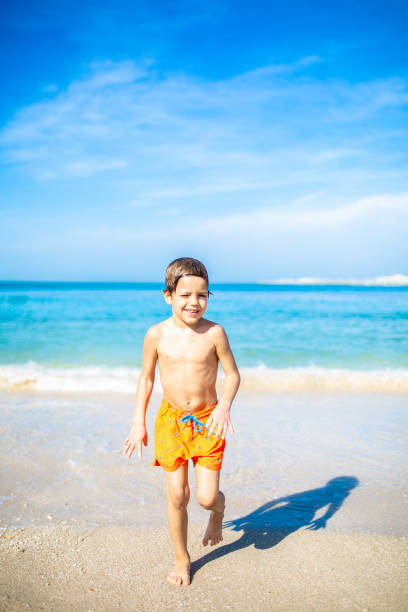 istock Little boy having fun on beach and being splashed by waves. Sunny summer day in Dubai Stock photo 1246039980