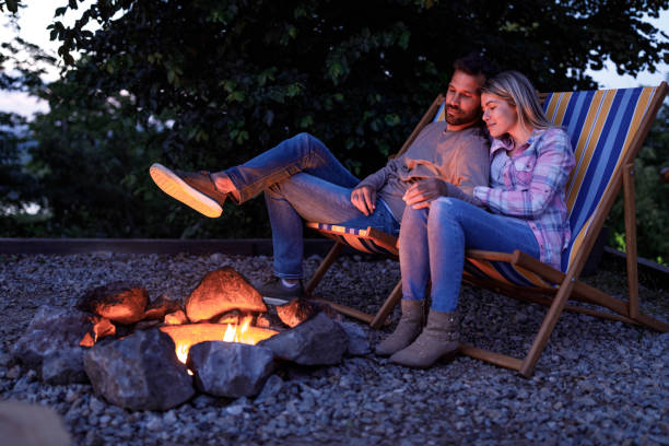 jeune couples aimants se relaxant dans des chaises de pont par le feu de joie. - camping friendship campfire fire photos et images de collection