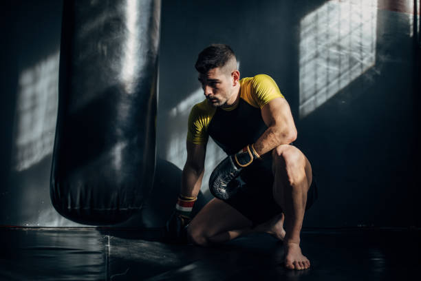 istock Man boxer crouching next to punching bag in gym 1246049952