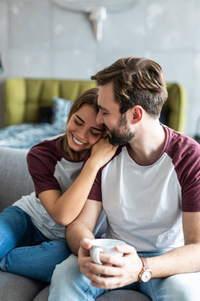 istock Beautiful young couple is talking and smiling while sitting on sofa at home. Man is holding a cup 1246059941