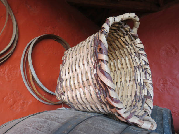 panier en osier avec poignées sur un baril de vin sur un fond rouge. fond rustique. garde-manger avec vieux baril de vin et panier en osier pour recueillir les raisins. - winery wine cellar barrel photos et images de collection