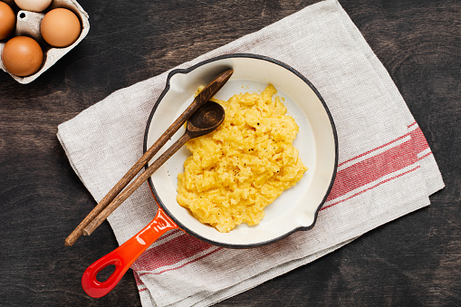 Scrambled eggs for breakfast on frying pan, dark wooden table background. Traditional English breakfast.Top view with cope space.