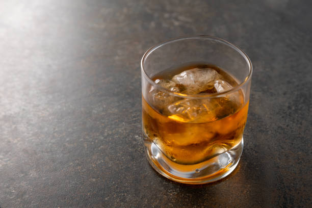 Glass of aged golden whiskey with ice cubes on the table. Amber colored alcohol beverage with rocks at the bar Glass of aged golden whiskey with ice cubes on the table. Amber colored alcohol beverage with rocks at the bar glass of bourbon stock pictures, royalty-free photos & images