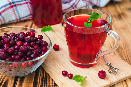 cranberry juice with mint in a glass cup on a bamboo board on a background of berries