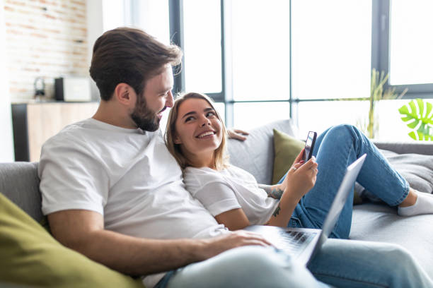 istock Beautiful young couple relaxing on a couch at home using laptop computer and mobile phone 1246120056