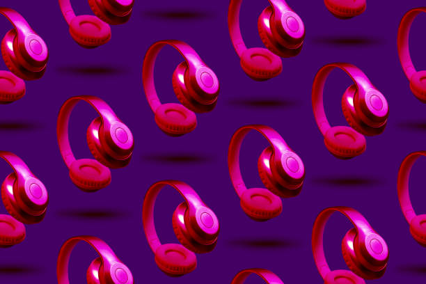 istock Neon pink metallic wireless headphones in the air on violet background. Horizontal pattern, site header in ultraviolet light 1246138282
