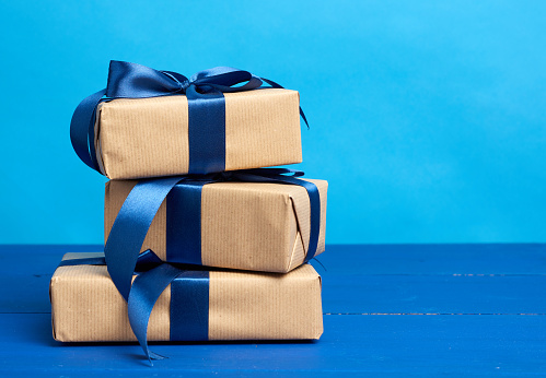 gifts in boxes wrapped in brown kraft paper and tied with silk ribbons on a blue background, festive backdrop for birthday, Christmas, copy space