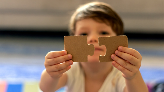 Puzzles in the hands of a child on colorful background.Boy at home playing with puzzles.Cute little child connecting a jigsaw pieces.Portrait of toddler holding jigsaw puzzle block,looking at camera.
