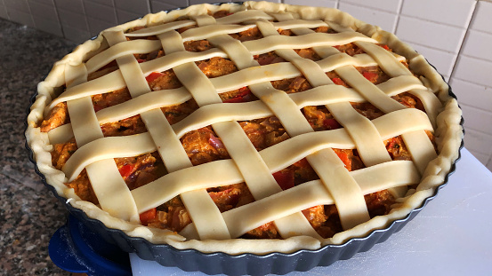 Stock photo of uncooked savoury chicken tikka pie in non stick pie tin on chopping board on kitchen worktop, lattice pastry top ready to be baked in oven under grill.