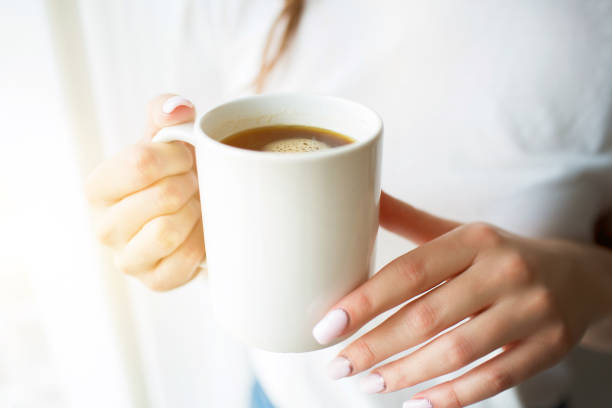 istock Young woman on kitchen during quarantine. Stand at window with curtains and hold white cup of tea or coffee. Close up. 1246180821