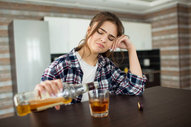 istock Young woman in kitchen during quarantin. Female alcoholic has social problems sitting drinking whiskey. Bored lonely woman pouring whiskey in glass. 1246180847