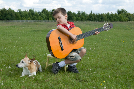 Young boy with Jack Russell terrier dog playing the guitar outside in a field