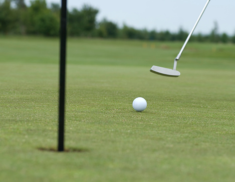 Putting shot in motion as golf ball is hit by golf club.