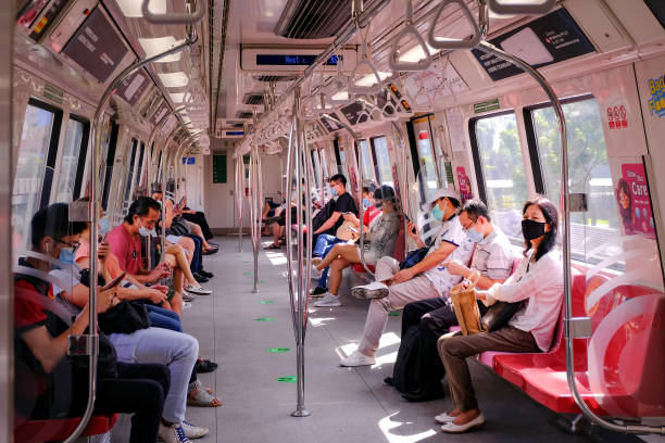 Passengers on uncrowded MRT train observing social distancing during coronavirus outbreak, Singapore Singapore May2020 COVID-19 MRT train. Passengers wearing masks on public transport. Train uncrowded during coronavirus outbreak. Social distancing observed; stickers and markings on floor. singapore mrt stock pictures, royalty-free photos & images