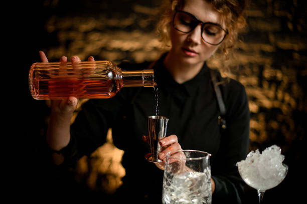 женщина бармен наливает ликер в стальной джиггер. - wine decanter elegance pouring стоковые фото и изображения