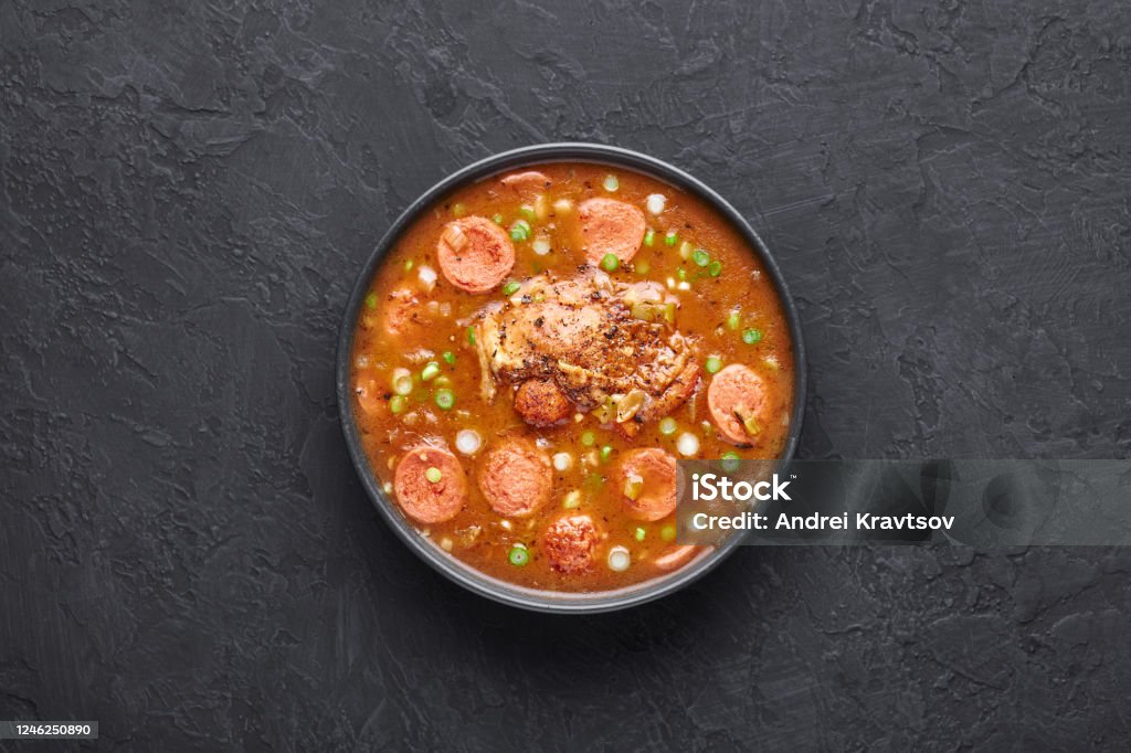 Chicken and Sausage Gumbo soup in black bowl on dark slate backdrop. Gumbo is louisiana cajun cuisine soup with roux. Chicken and Sausage Gumbo soup in black bowl on dark slate backdrop. Gumbo is louisiana cajun cuisine soup with roux. American USA Food. Traditional ethnic meal Food Stock Photo