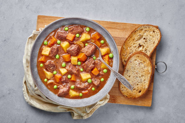 istock Irish Beef Stew with bread in matt gray bowl on concrete background. Stew with beef or lamb meat with potatoes, carrots, peas and herbs. Traditional american and european food. Dinner meal 1246250891