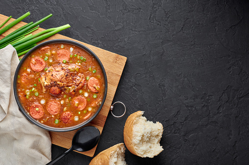 Chicken and Sausage Gumbo soup in black bowl on dark slate backdrop. Gumbo is louisiana cajun cuisine soup with roux. American USA Food. Traditional ethnic meal. Copy space