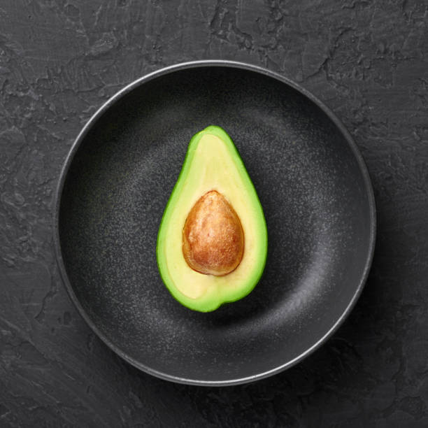 half avocado in black rough bowl on dark slate backdrop. black ceramic dish setting - 18639 imagens e fotografias de stock