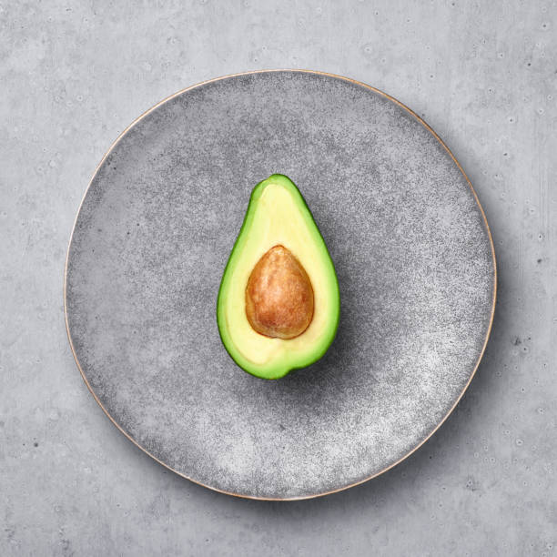 Half Avocado in gray hand made matte plate on concrete rough backdrop. Grey ceramic saucer setting.