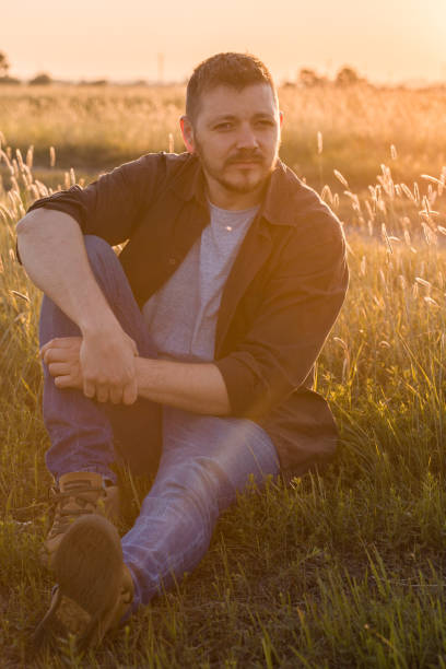 istock Hipster on dreamy face sits on grass. Guy looks.  Man with long beard and mustache, defocused green meadow background. 1246256963